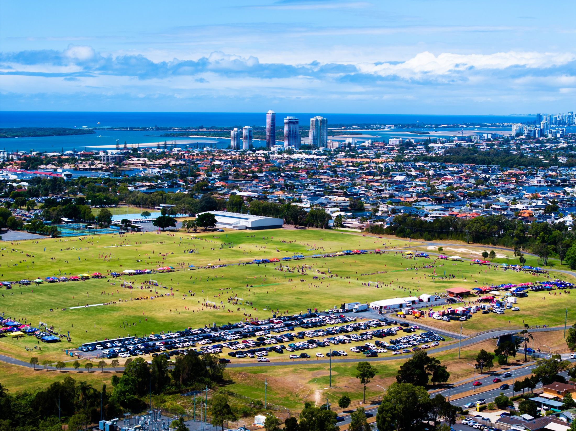 Aerial view of the All Schools fields at Runaway Bay, packed with teams and marquees, with the Gold Coast skyline and Broadwater behind